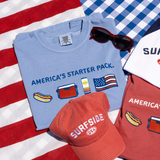 Light blue t-shirt with 'America's Starter Pack' featuring a hotdog, red cooler, a Surfside can, and an American Flag text and graphics, red cap with 'Surfside USA' text, red sunglasses, and red t-shirt with similar graphics on an American flag background.