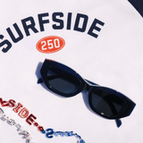 Dark blue sunglasses on a white surface with 'Surfside' branding.