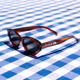 Red cateye frame sunglasses and red accents on a blue and white checkered background