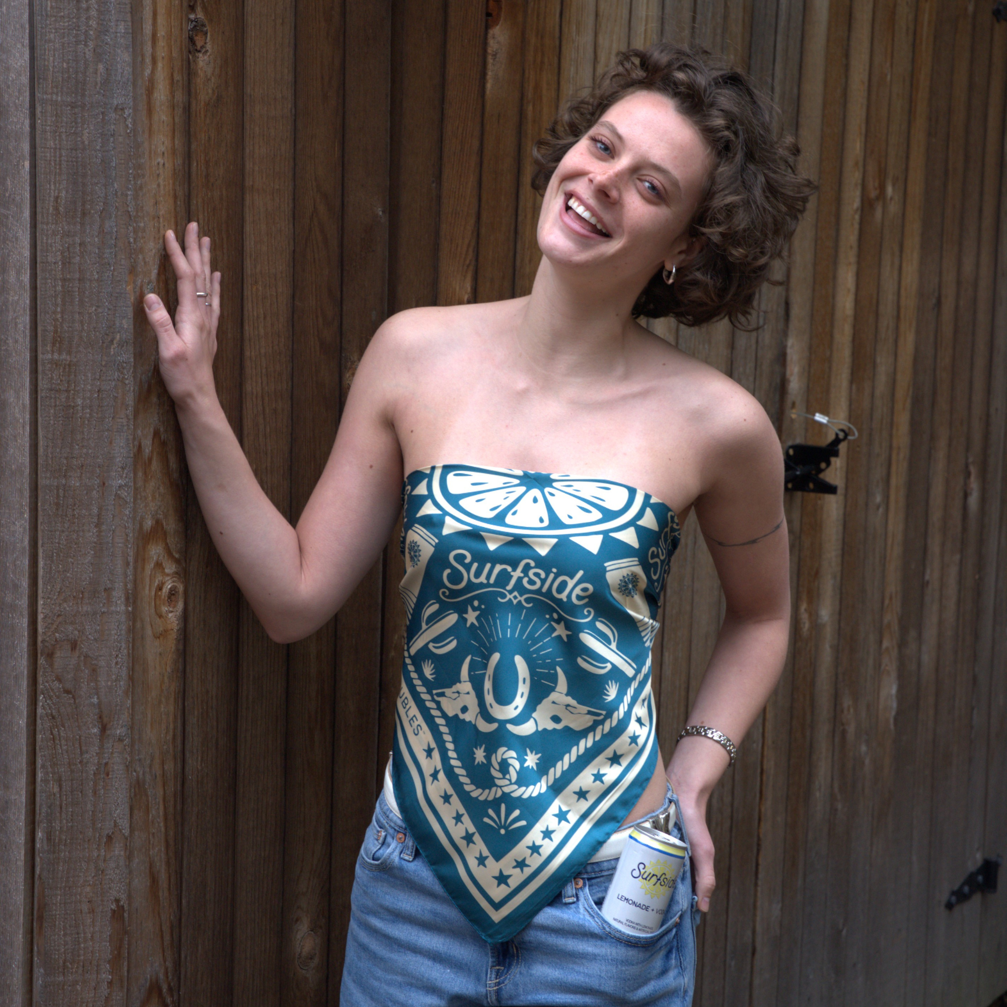 Woman wearing a strapless green bandana top with 'Surfside' design against a wooden background