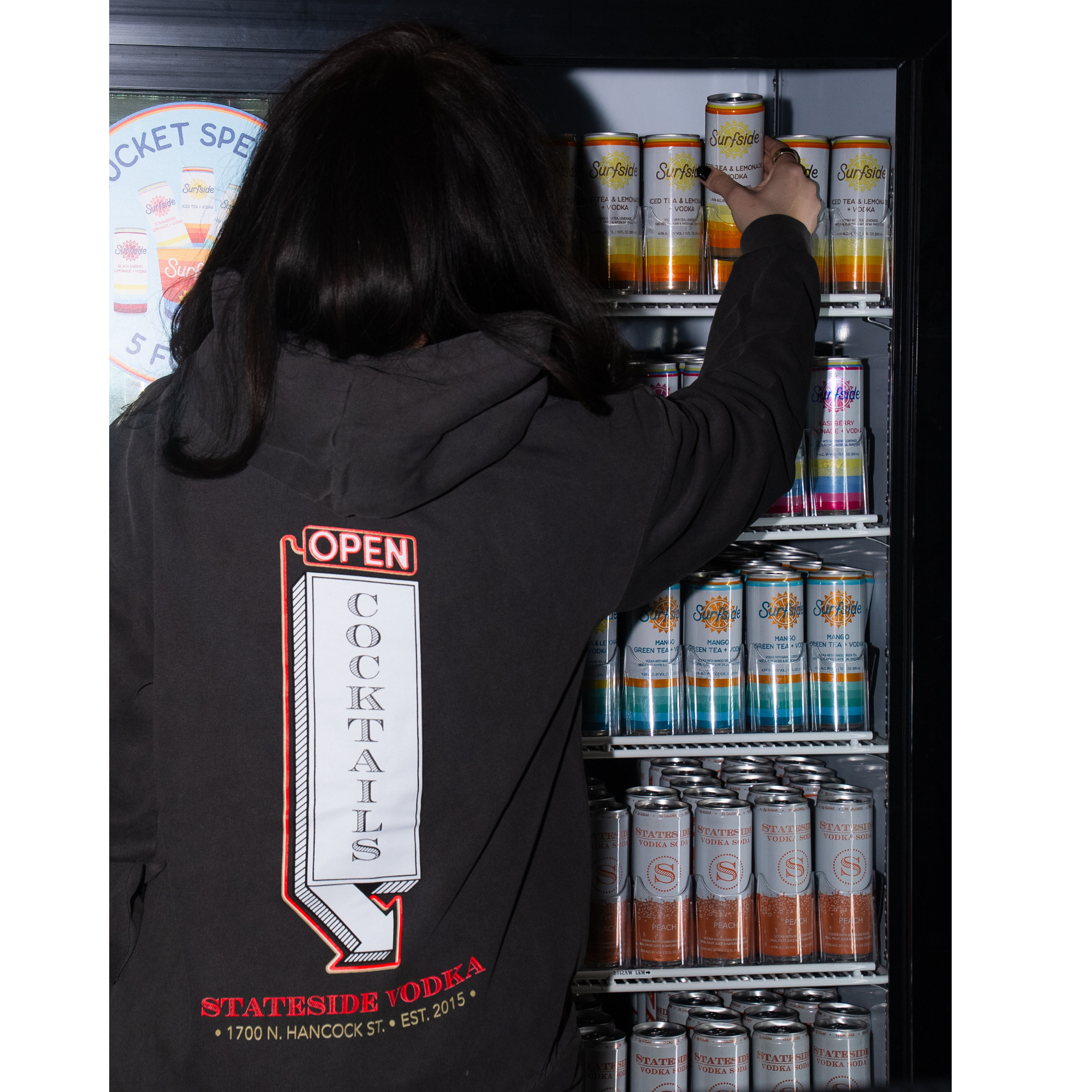 Person reaching into a refrigerator filled with Surfside cans, wearing the LED Stateside Vodka 