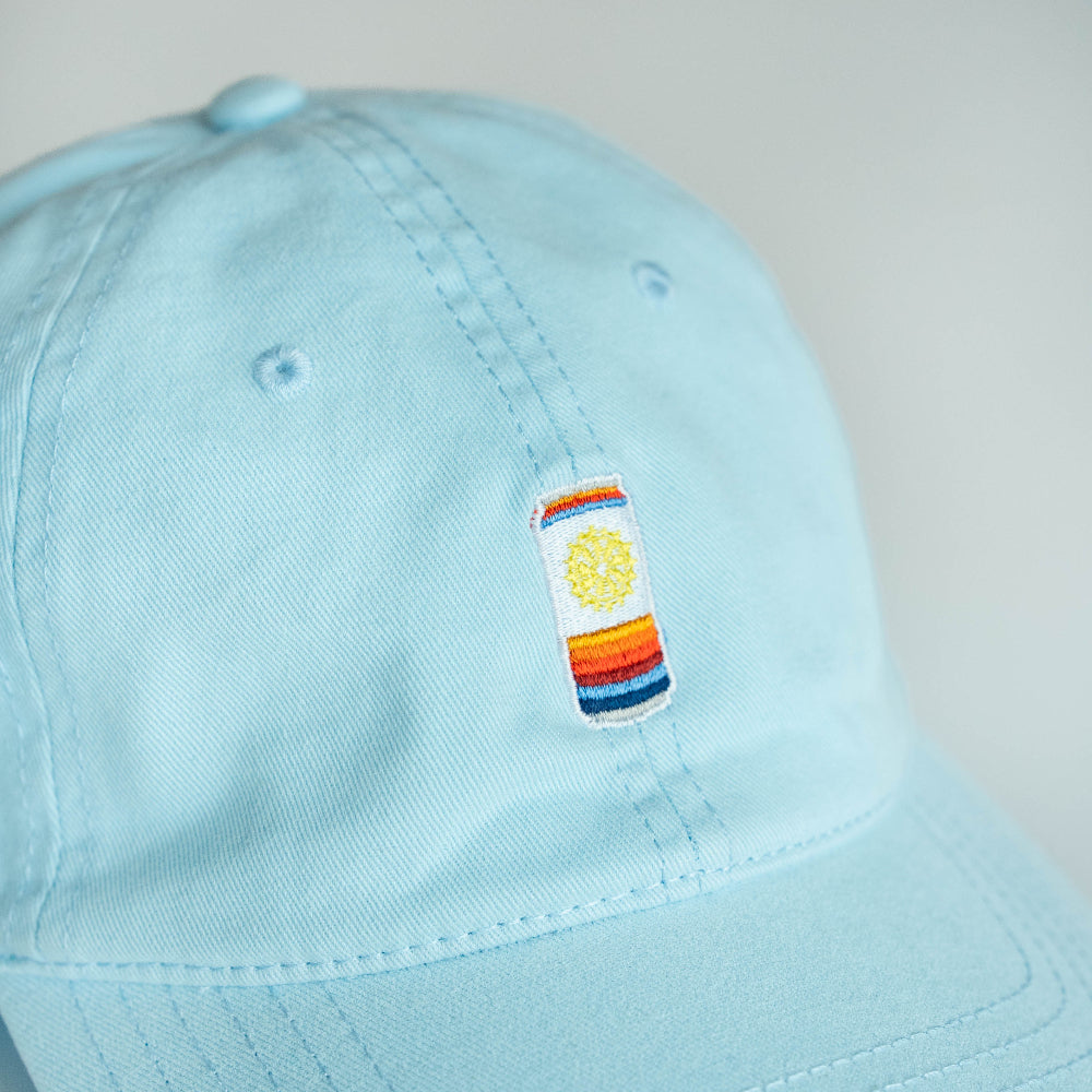 Light blue cap with a colorful embroidered can patch on a neutral background