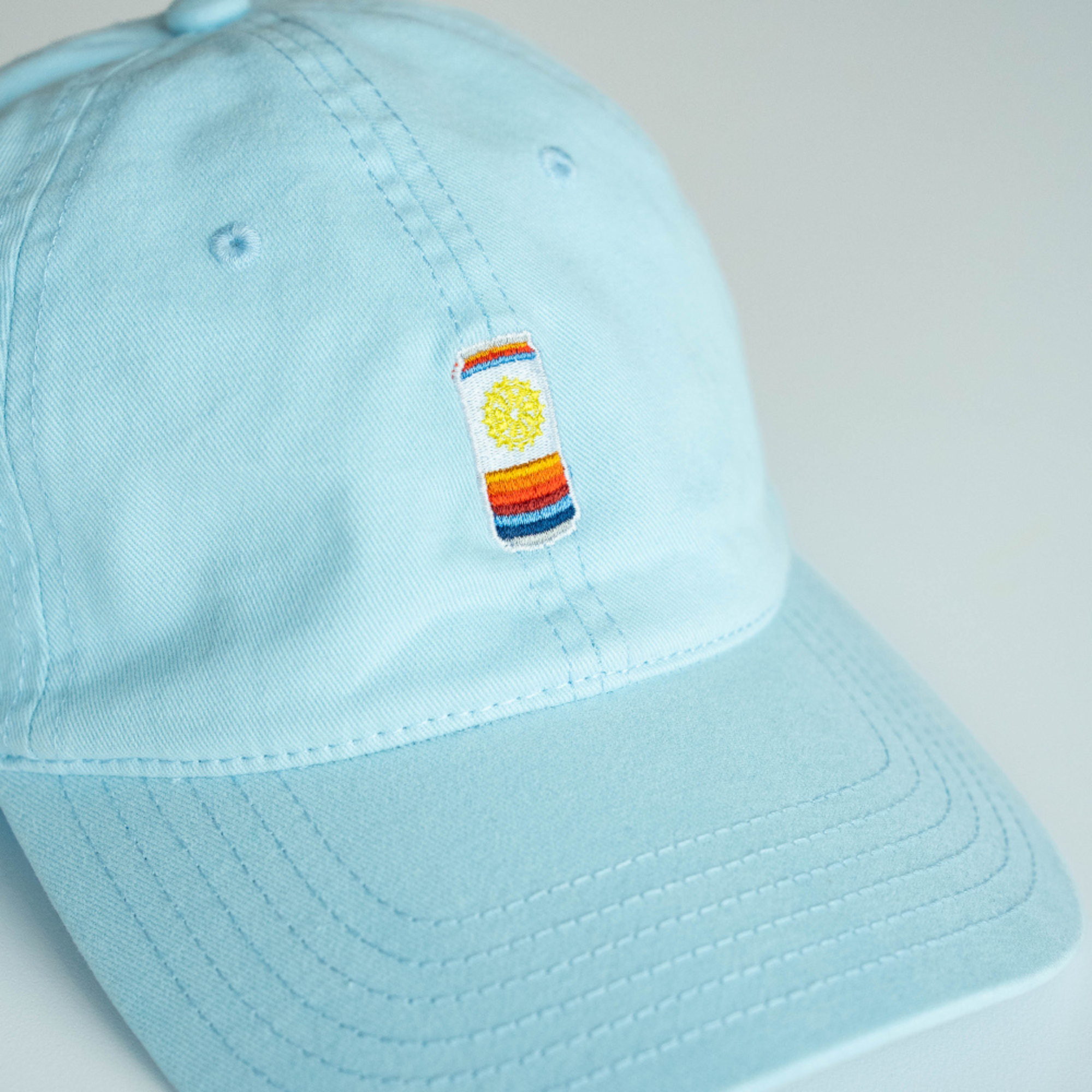 Light blue cap with a colorful embroidered can patch on a light gray background