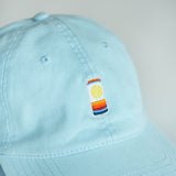 Light blue cap with a colorful embroidered can patch on a neutral background