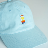 Light blue cap with a colorful embroidered can patch on a light gray background