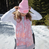 Person wearing a pink beanie and pink patterned Surfside scarf in a snowy forest