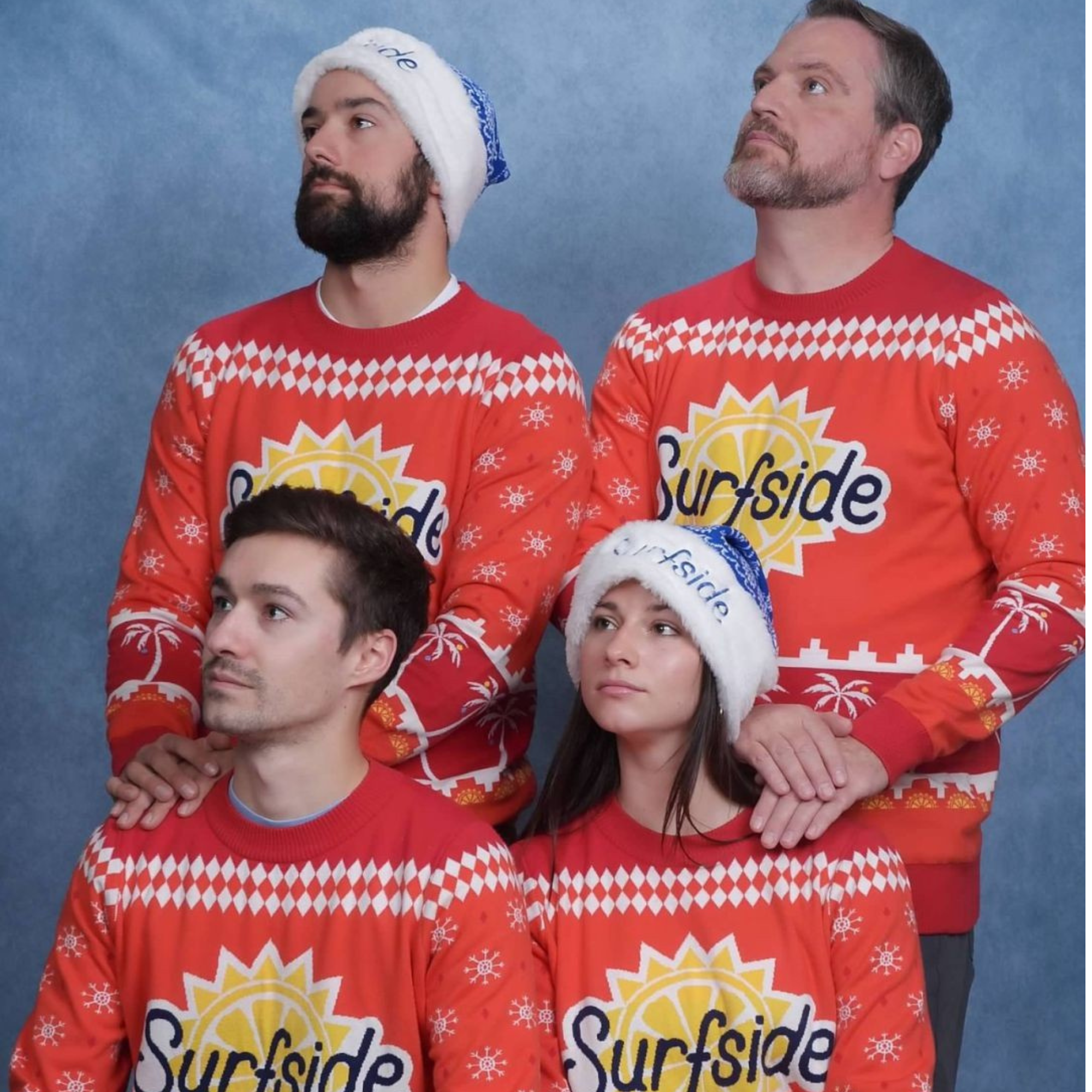 Four people wearing matching red Surfside Christmas sweater, with two men standing behind and two women in front, all featuring the Surfside logo and a white Santa hat on one of the men.