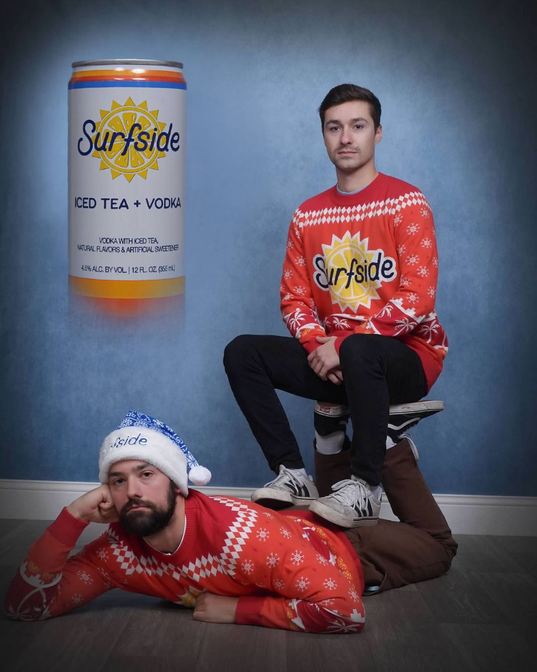 Two people wearing Surfside-themed red holiday sweaters with a can of Surfside Iced Tea and Vodka in the background.