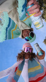 Two people holding Surfside cans looking down with the Surfside colorful scarves around their neck and in the background there's a blue sky