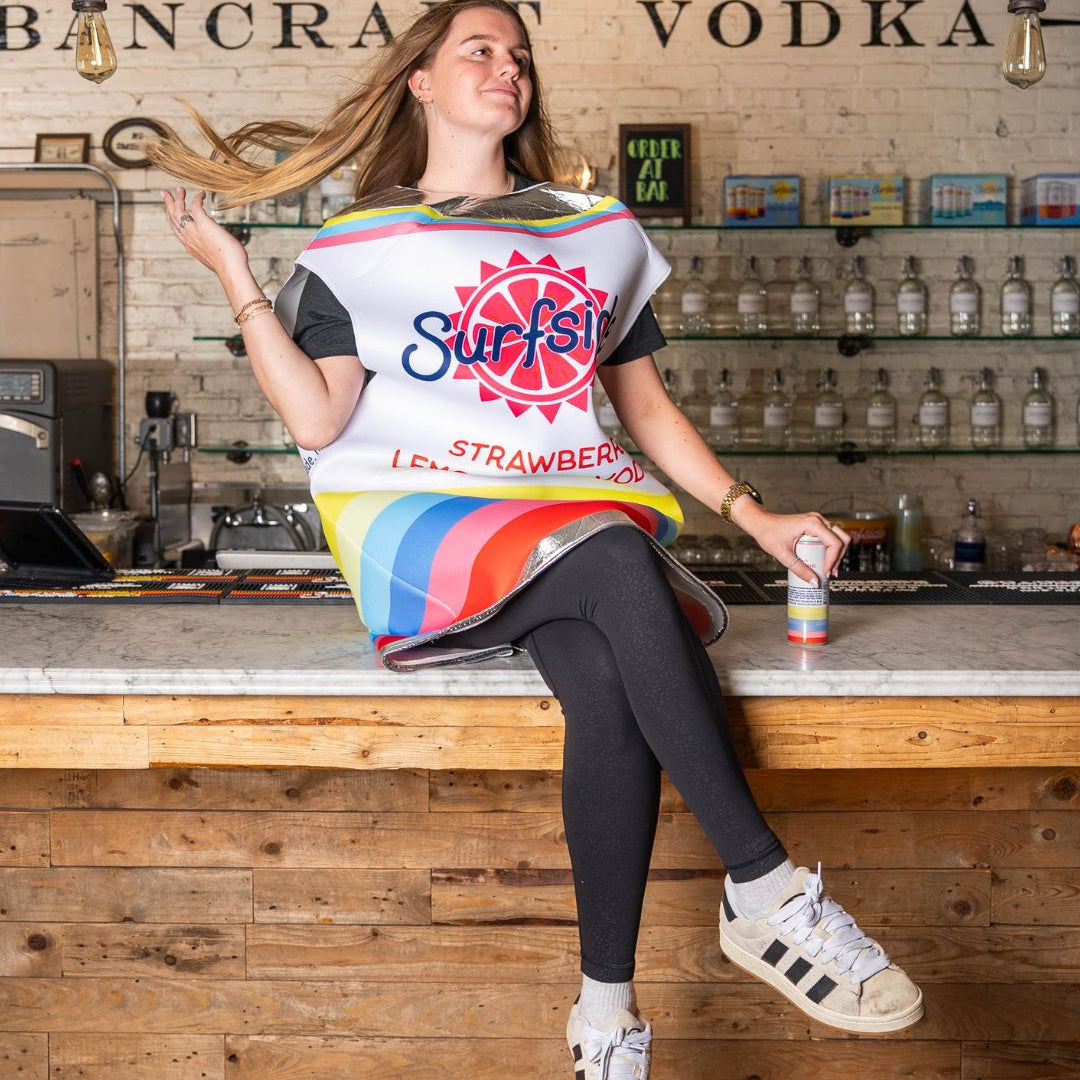 Person sitting on a bar wearing a Surfside Strawberry Lemonade can costume with Surfside's brand logo, holding a can of Surfside