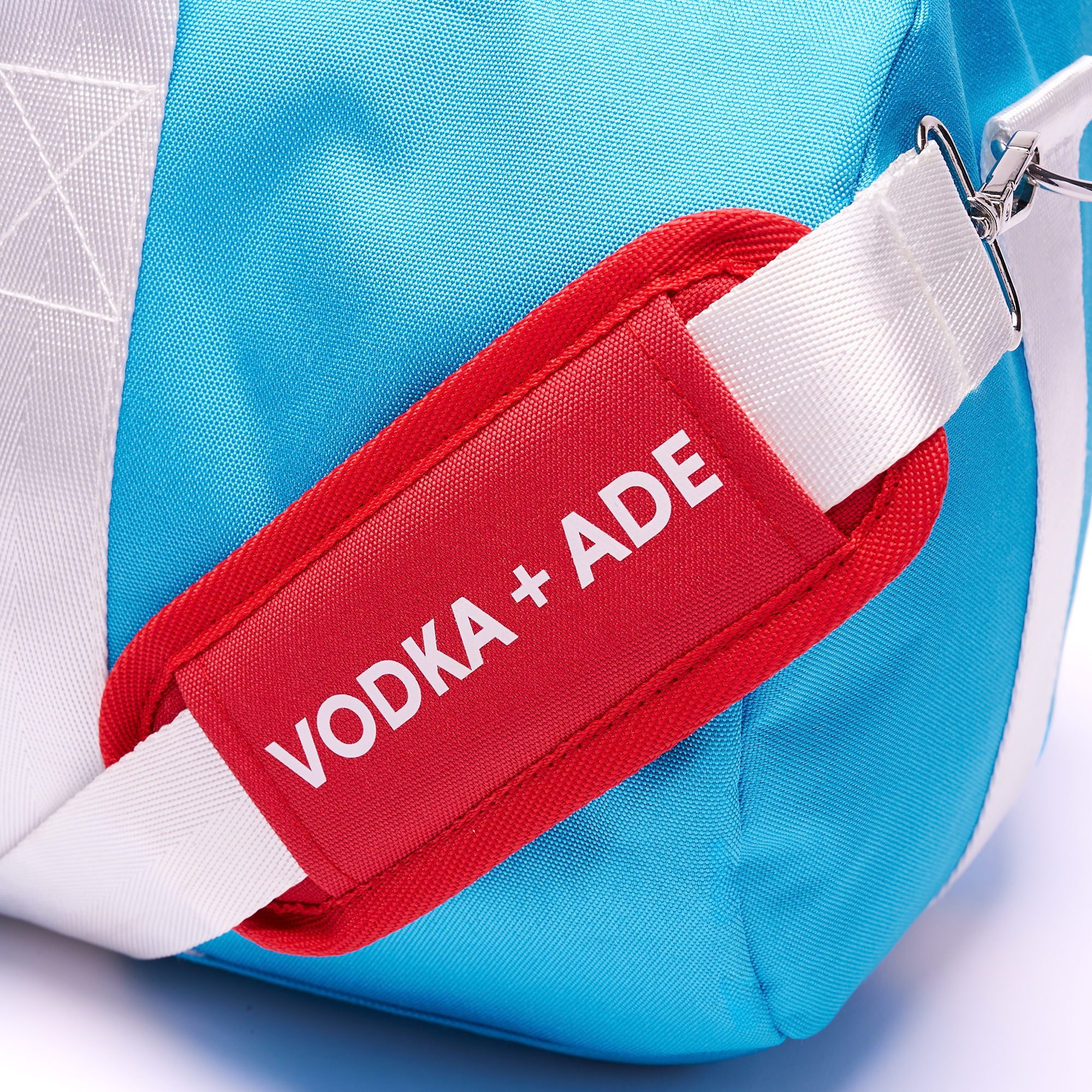 Close up of the shoulder strap showing Vodka + Ade the red shoulder strap pad is showing on the white regular duffel bag strap