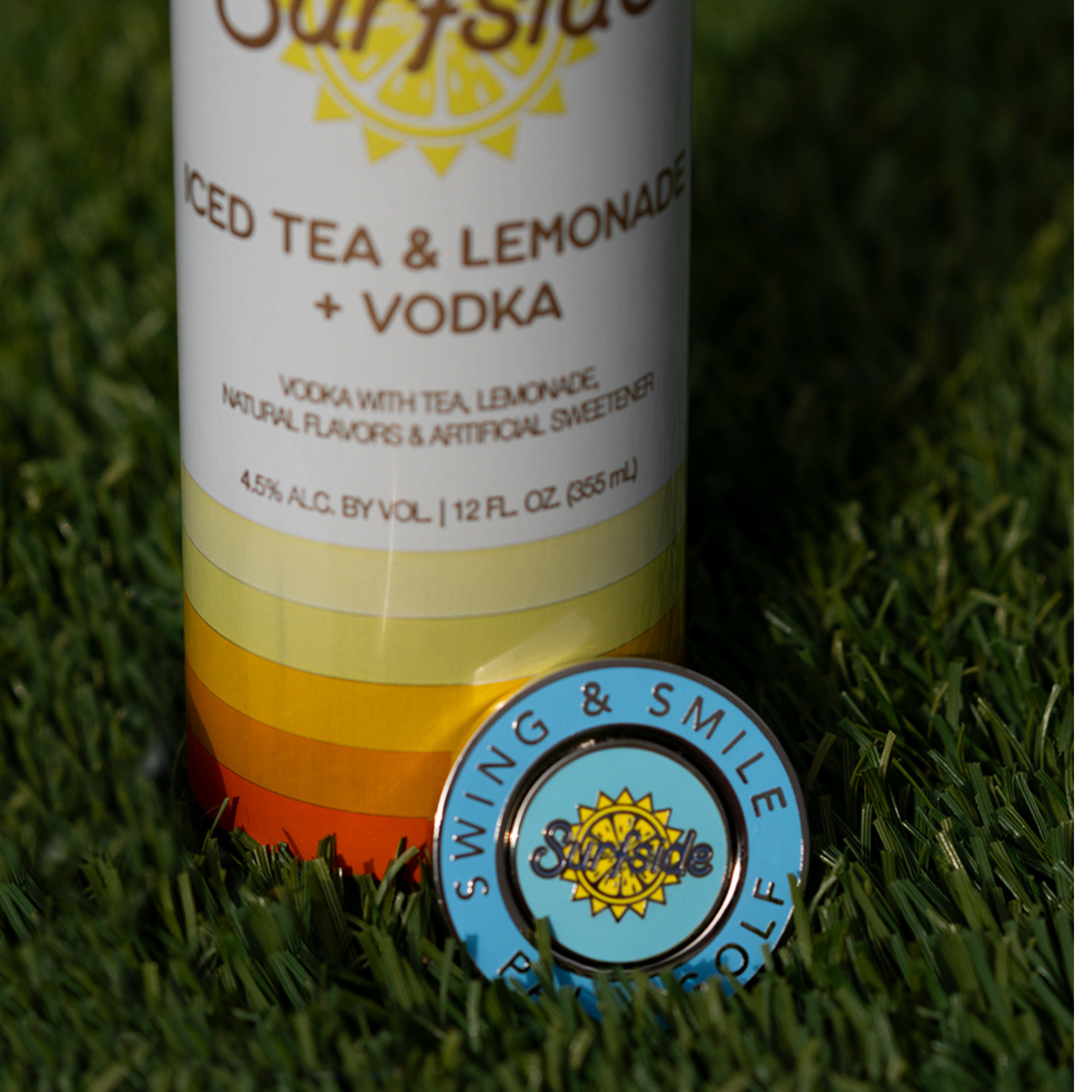 Surfside and Palm Golf Collaboration Ball marker resting in the grass on a Ice Tea and Lemonade and Vodka Surfside branded can