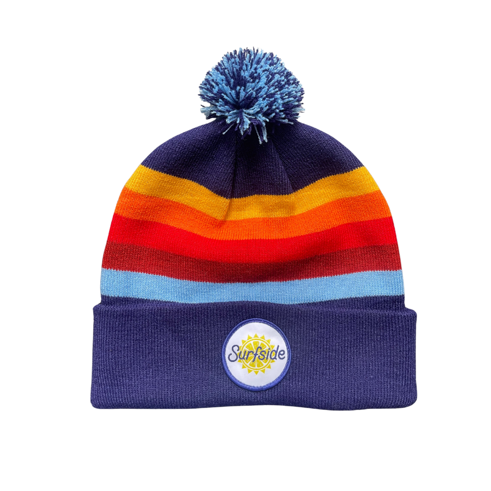 A striped Surfside winter beanie with a pom-pom on top, featuring colors blue, red, orange, and yellow, and a Surfside sewn on logo on the front.