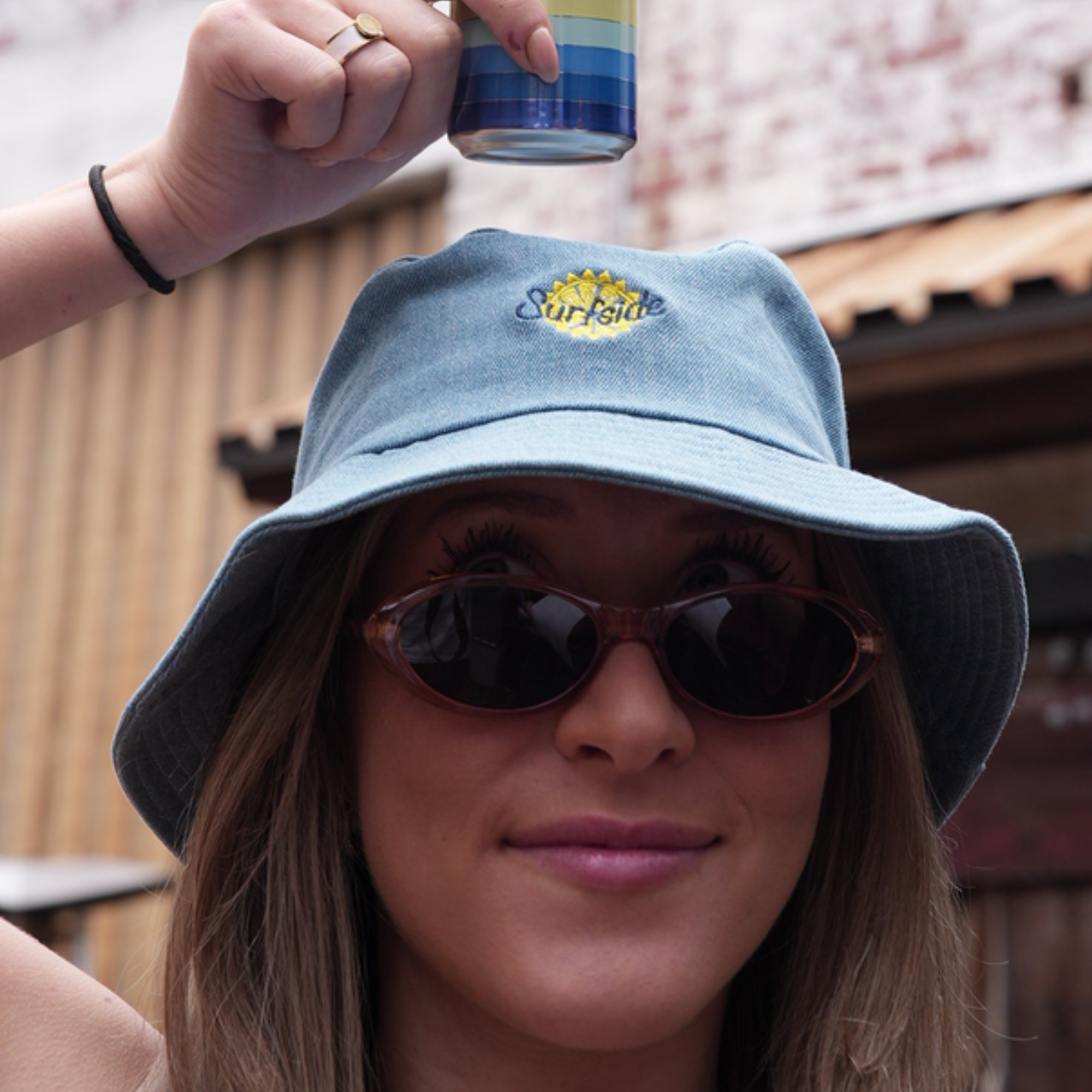 Person wearing a Surfside blue denim bucket hat with 'Surfside' logo, holding a colorful can