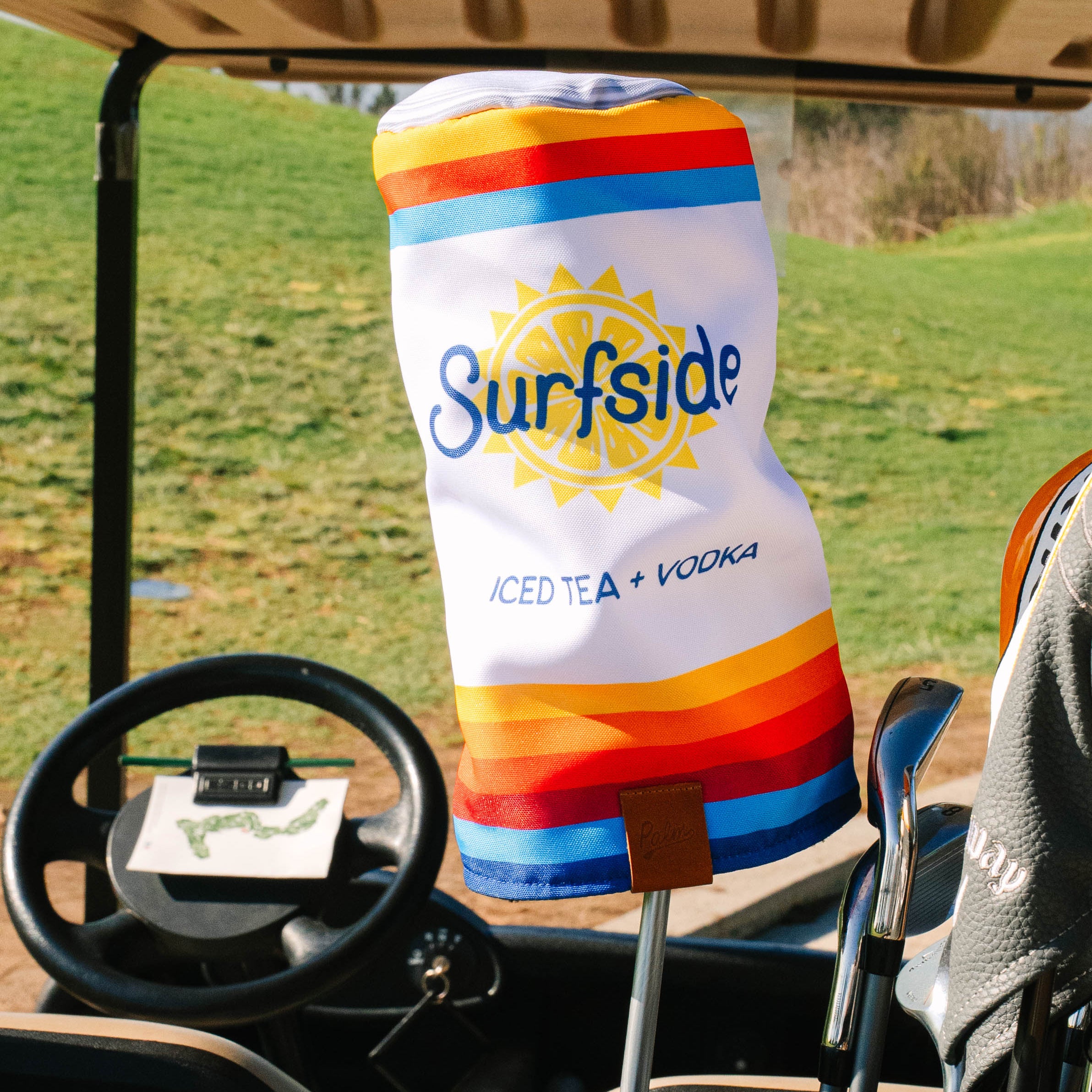 Surfside Iced Tea Can Gold Driver cover in a golf cart with grass and sky in the background