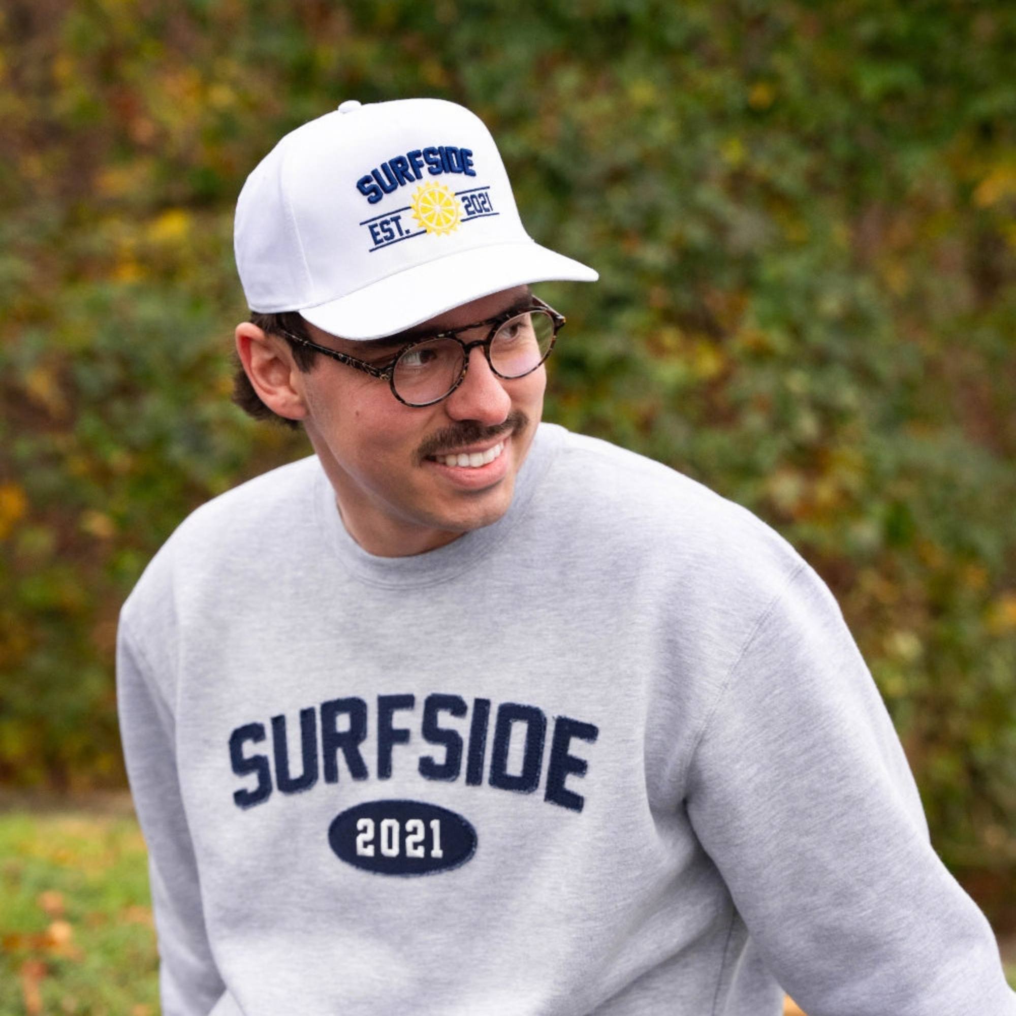 Person wearing a white Surfside Est. 2021 hat and gray sweatshirt with 'Surfside 2021' text outdoors.