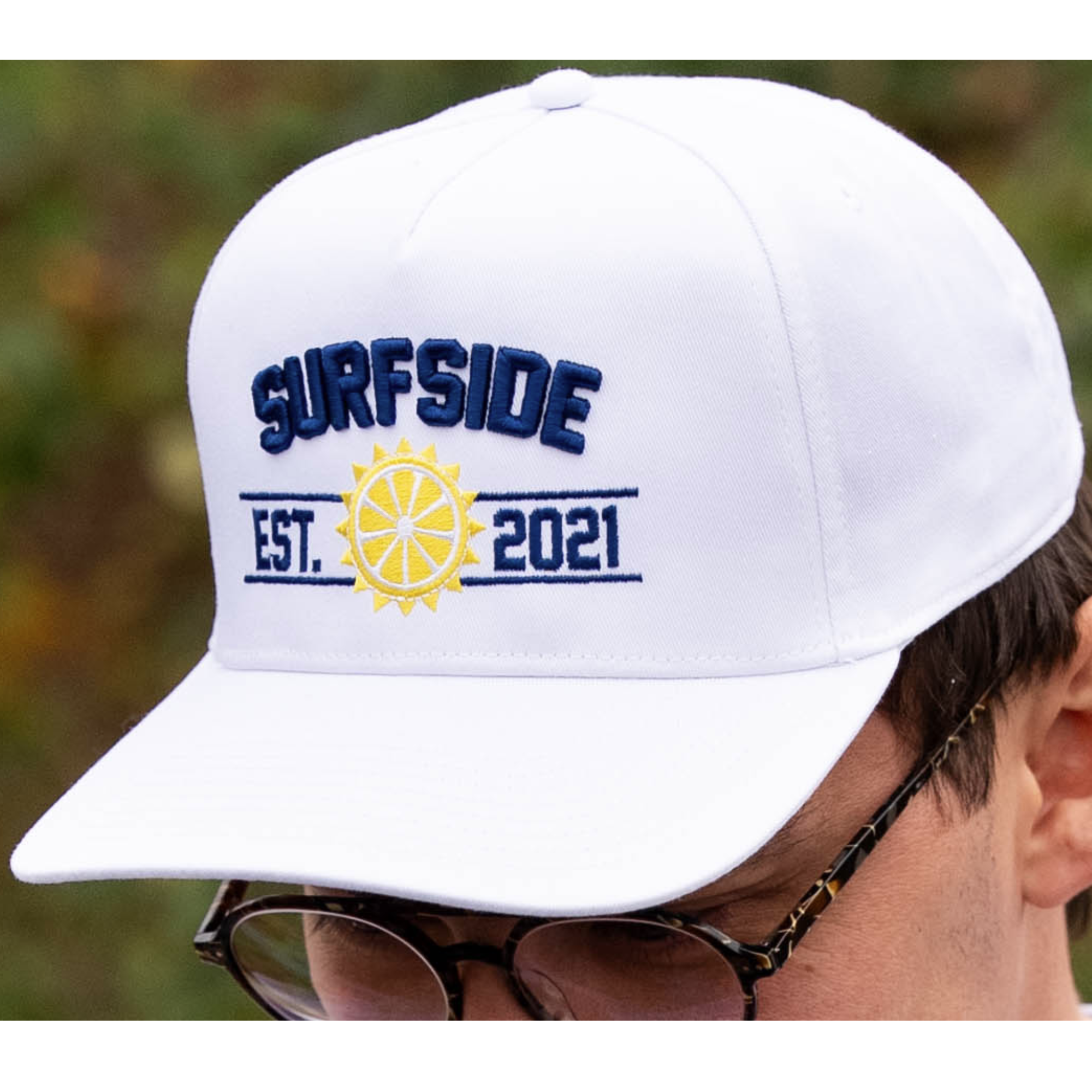 White cap with 'Surfside Est. 2021' text and logo, worn by a person outdoors.