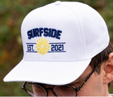 White cap with 'Surfside Est. 2021' text and logo, worn by a person outdoors.