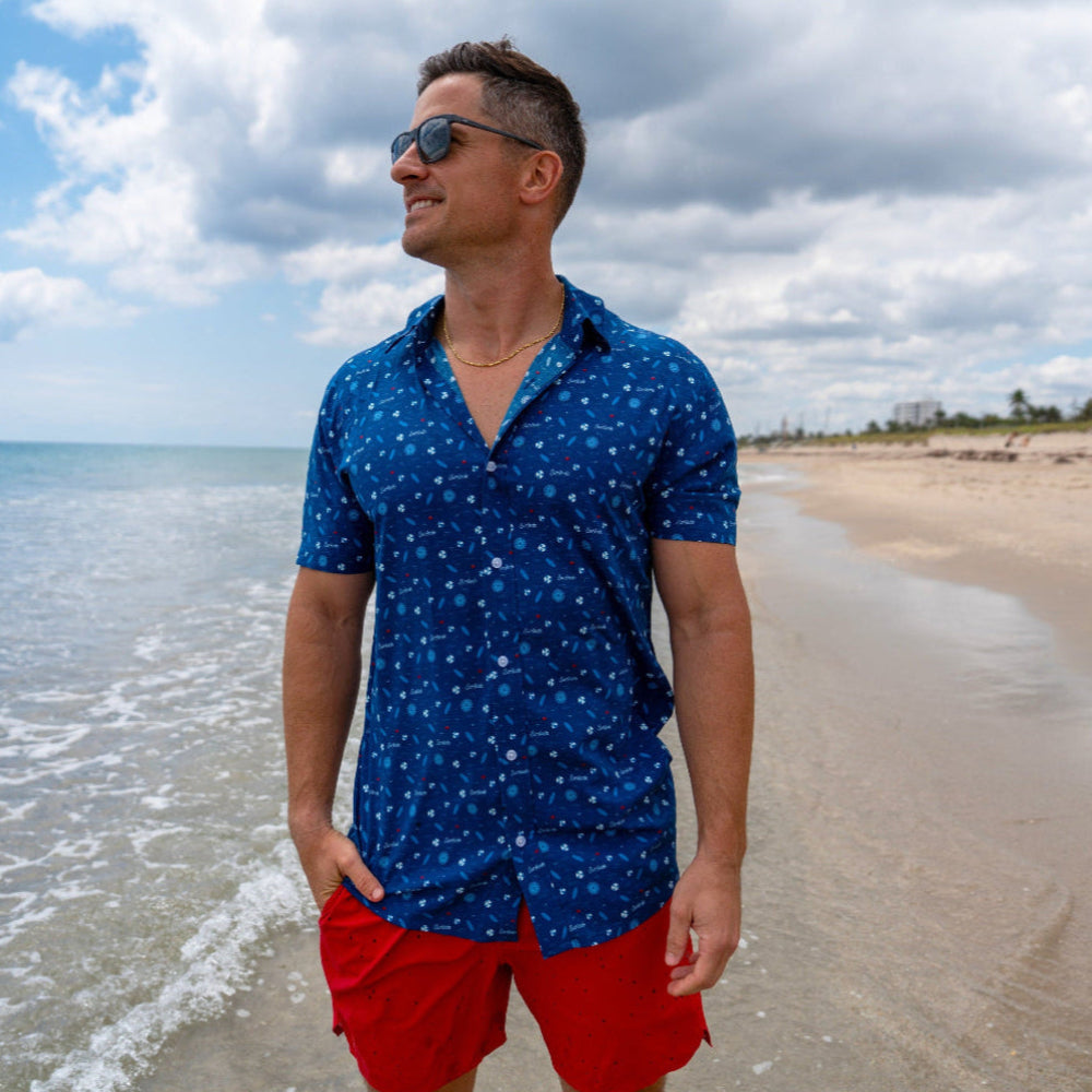Man wearing the Surfside Hawaiian inspired button down shirt with red shorts and sunglasses in a beach setting 