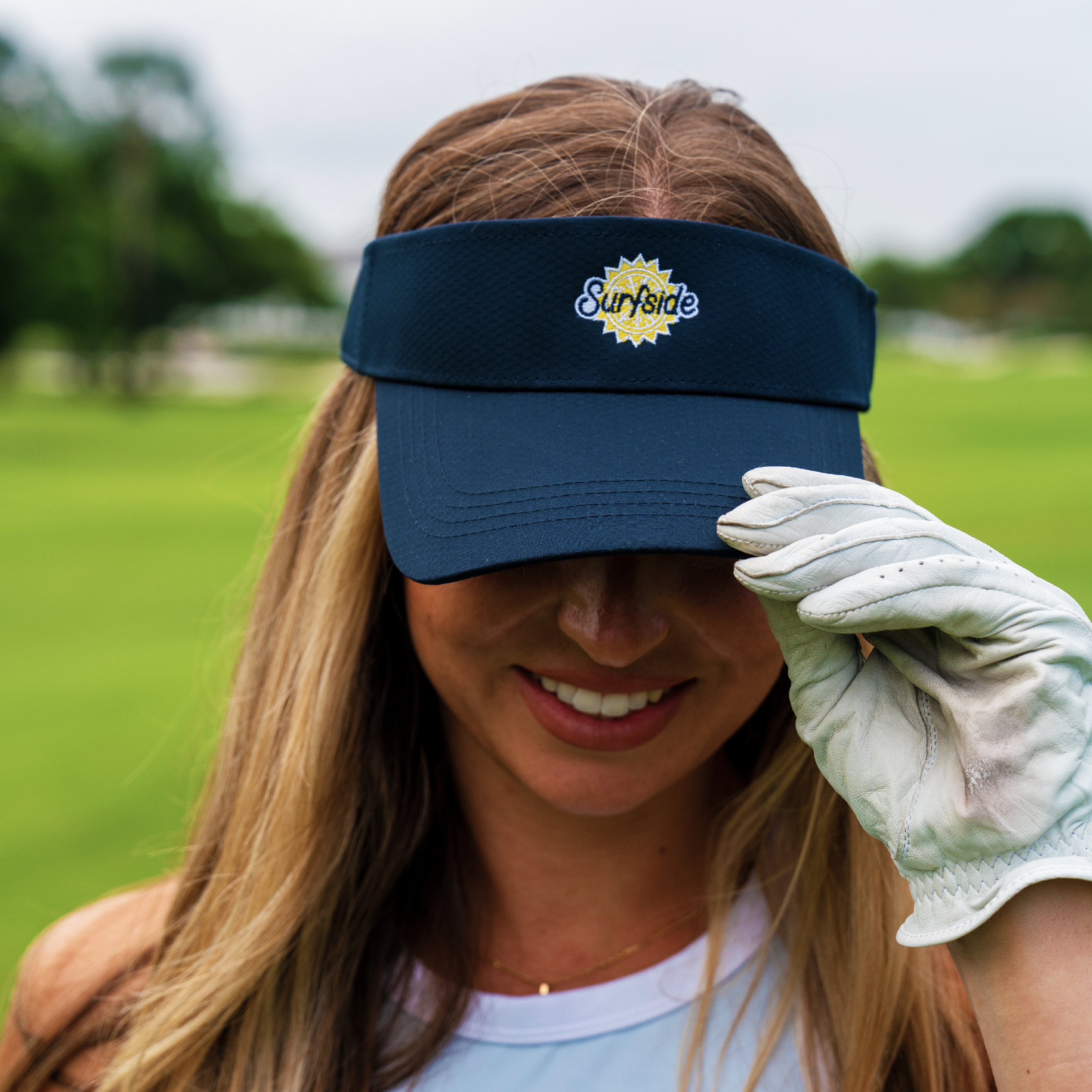 Women holding  navy blue visor featuring Surfside logo with white golf glove in an outdoor setting