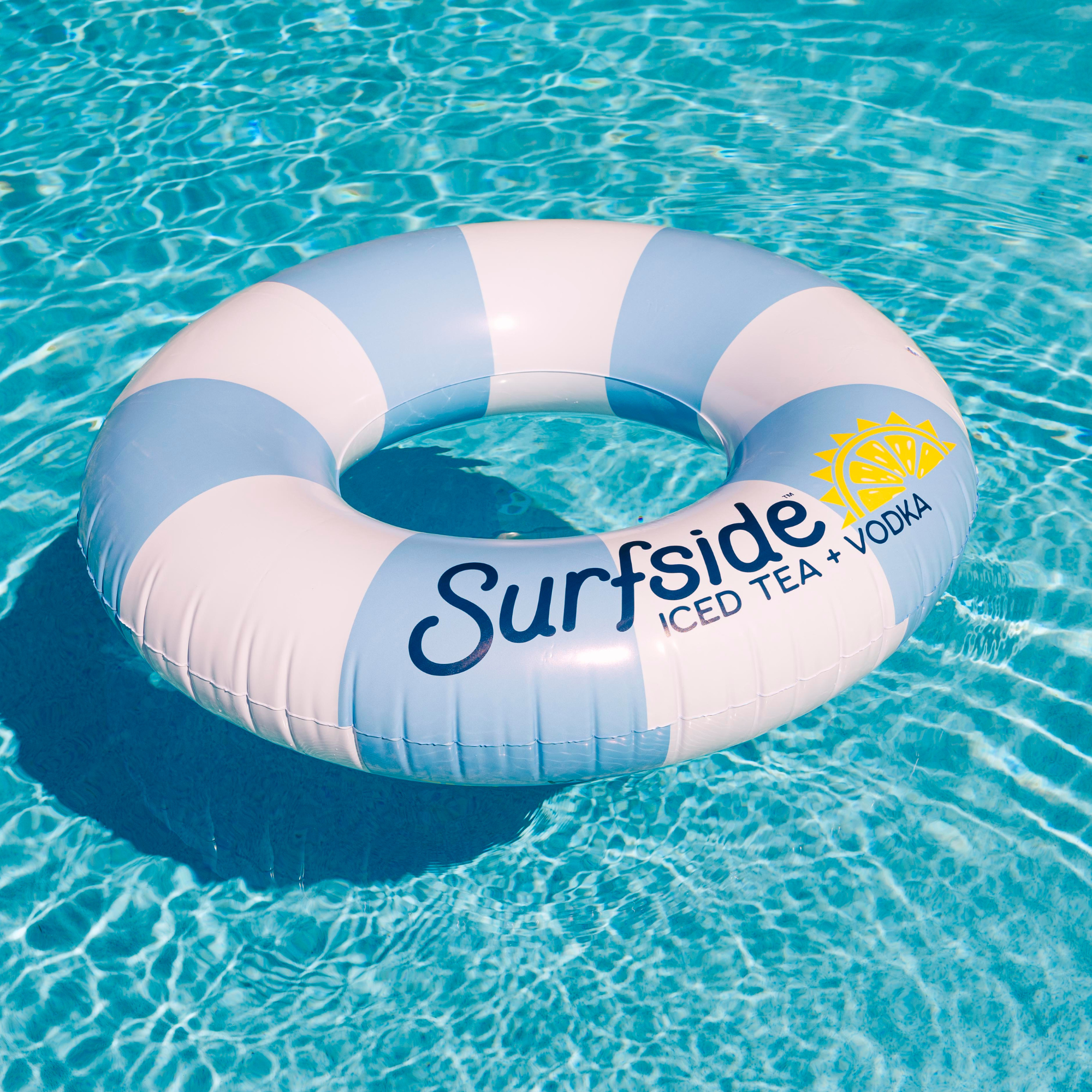 An inflatable pool float with blue and white stripes, featuring the text 'Surfside ICED TEA + VODKA' and a yellow sun graphic, floating on clear turquoise pool water.