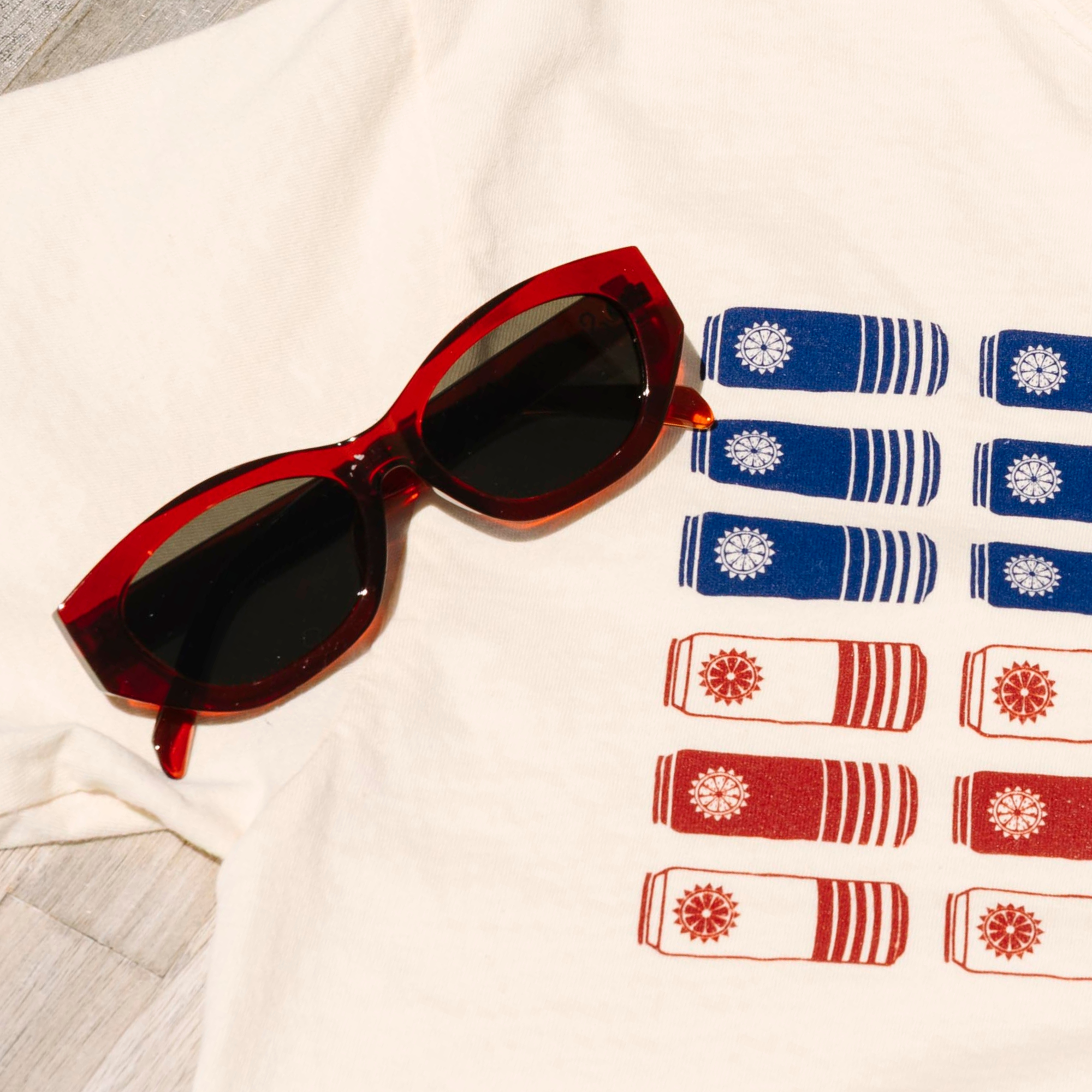 Red cateye sunglasses on a cream t- shirt that features red, white and blue surfside cans