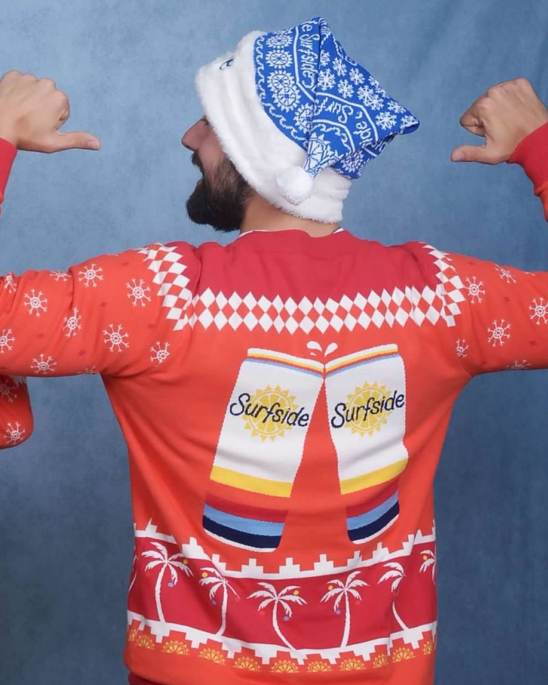 Person wearing a red Surfside can-themed red sweater with a blue and white holiday hat on a blue background
