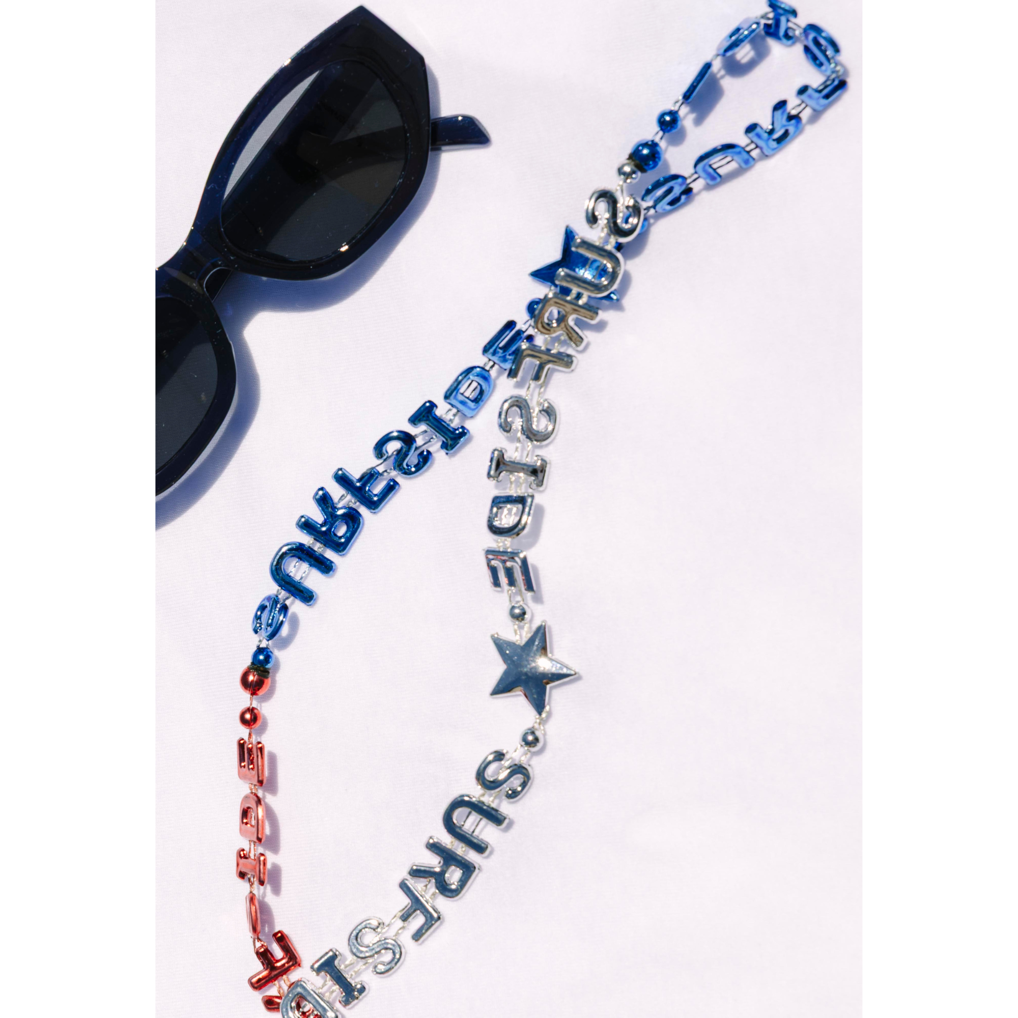 Surfside red, silver and blue necklace with Blue cat eye sunglasses laying on a white background