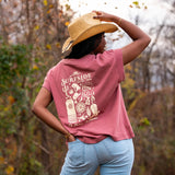 Person wearing a faded red t-shirt with a Surfside Western themed graphic, standing outdoors with trees in the background.
