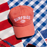 Red dad hat with 'Surfside USA' text on a checkered tablecloth with American flag pattern