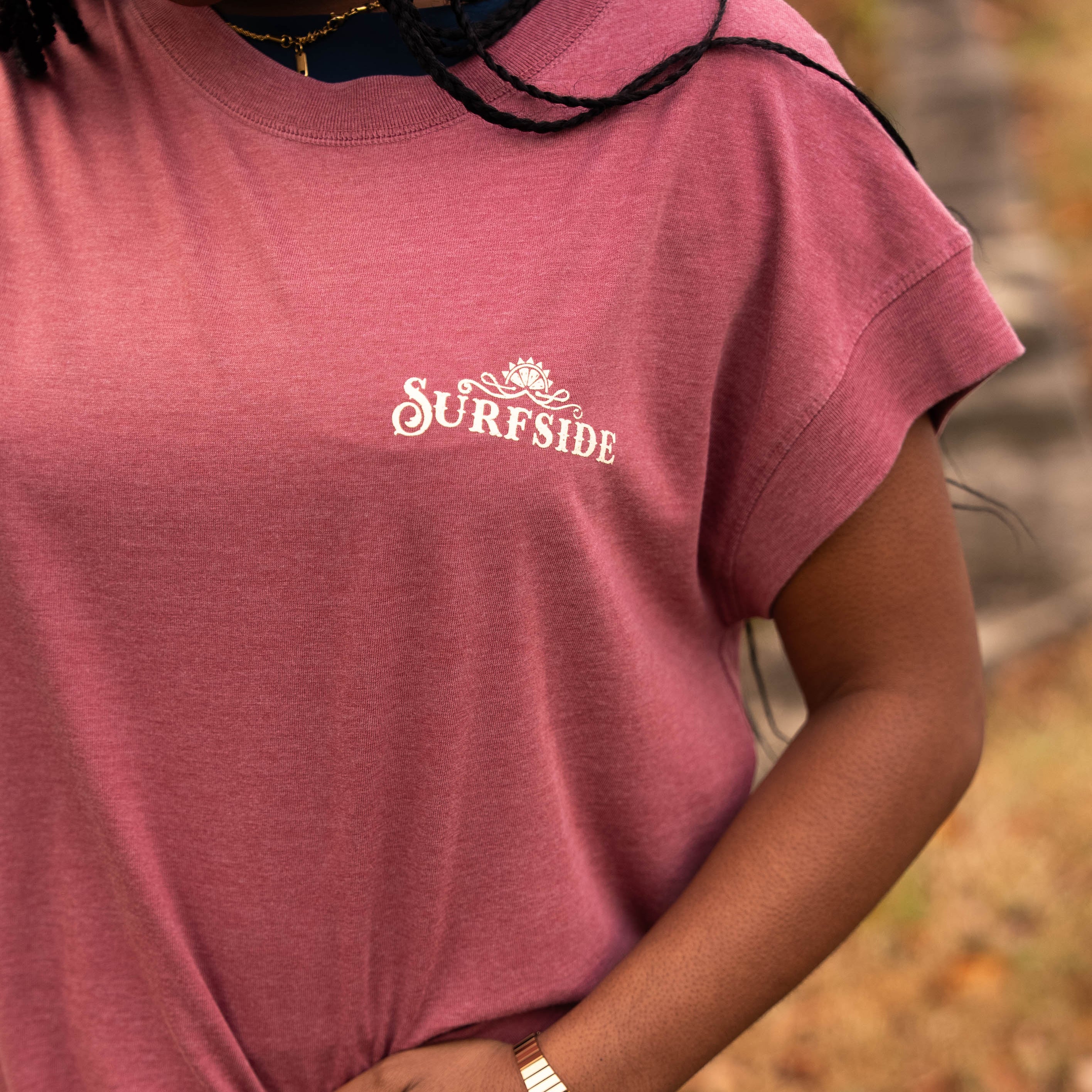Person wearing a faded red 'Surfside' western inspired t-shirt with a blurred natural background