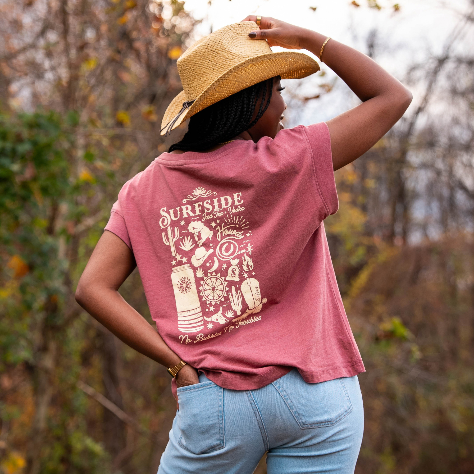 Person wearing a faded red t-shirt with a Surfside Western themed graphic, standing outdoors with trees in the background.