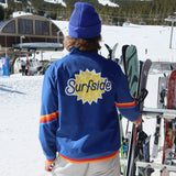 Person wearing a blue 'Surfside' windbreaker with skis in a snowy mountain setting