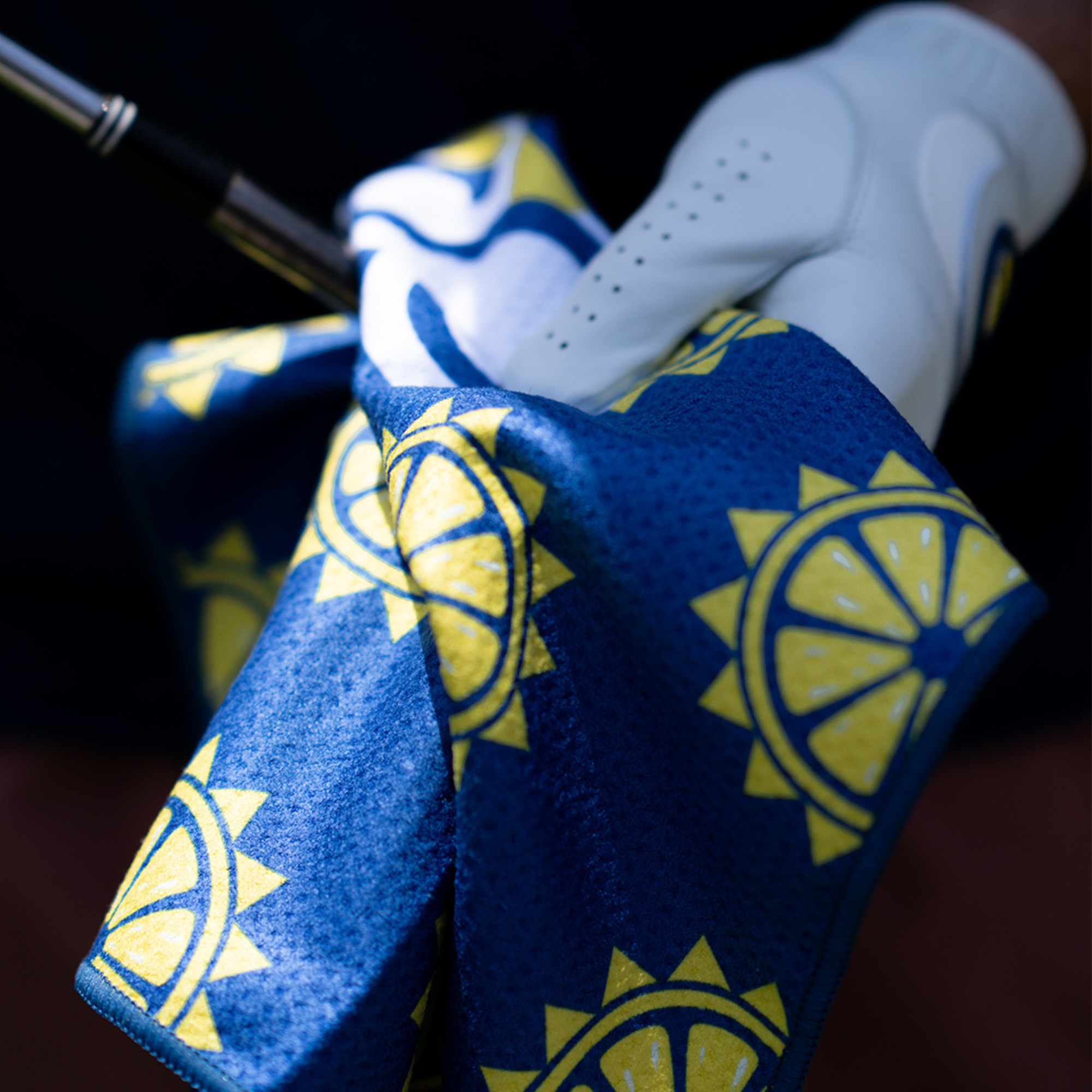 Navy blue and sun logo Golf Towel being held with white golf glove and cleaning a golf club