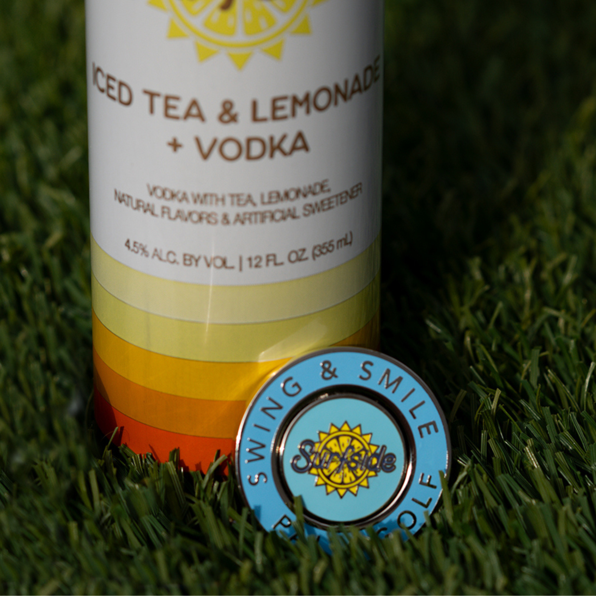 Surfside and Palm Golf Collaboration Ball marker resting in the grass on a Ice Tea and Lemonade and Vodka Surfside branded can