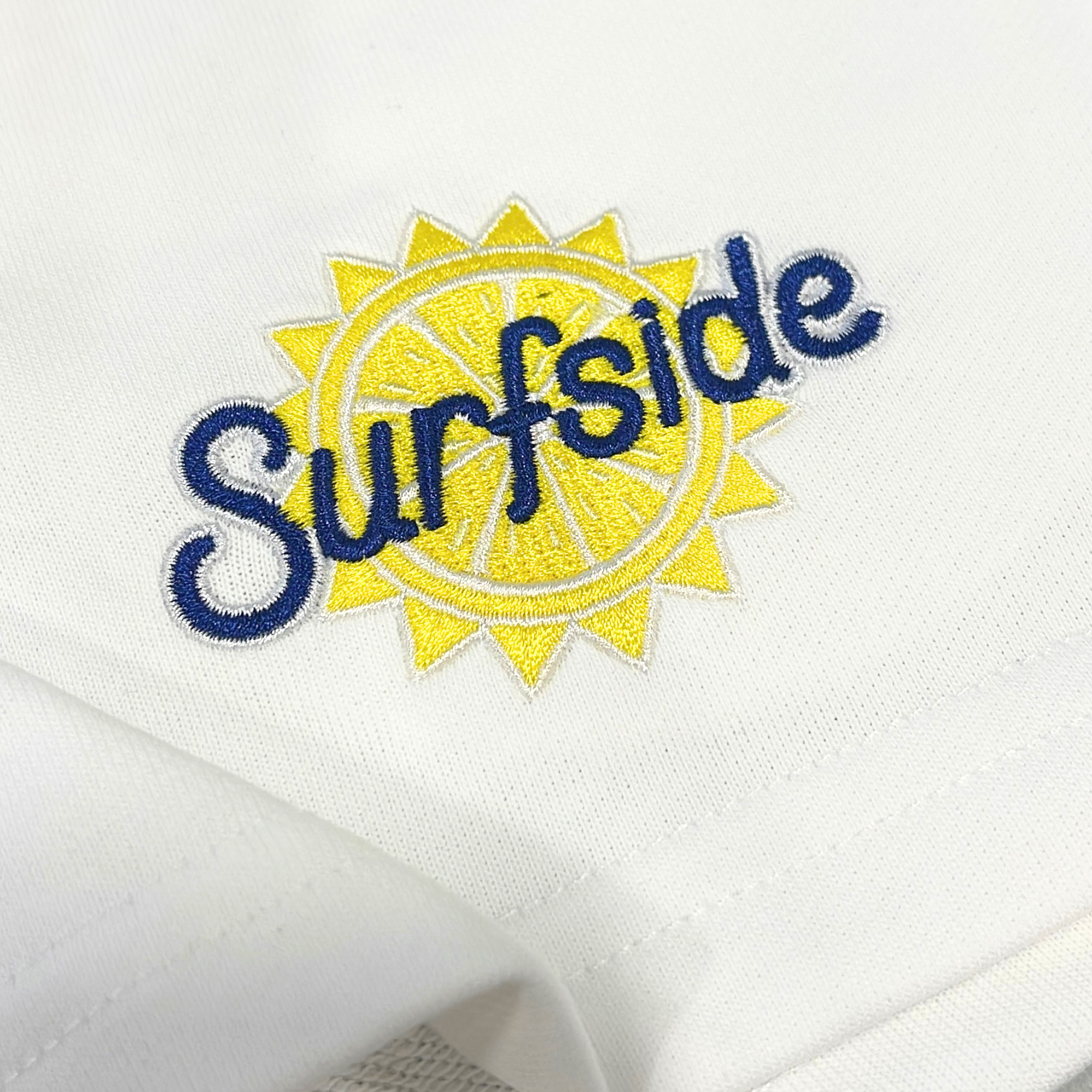 Close up of embroidered 'Surfside' logo on a white sweat shorts 