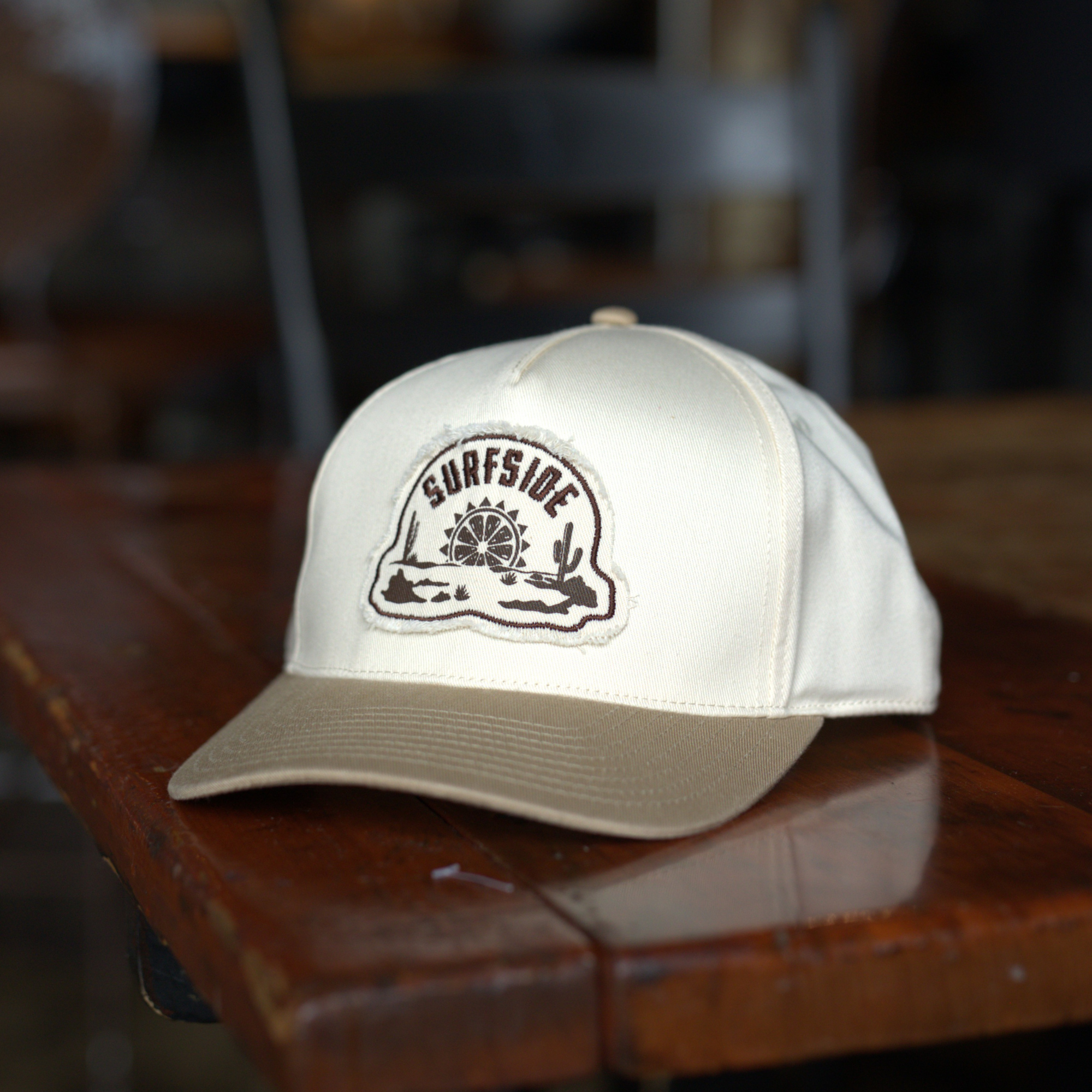 White and cream snapback hat featuring a western style Surfside logo embroidered patch sitting on a wood table 